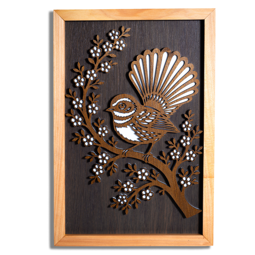 Fantail pīwakawaka layered timber wall art in a macrocarpa frame, front view